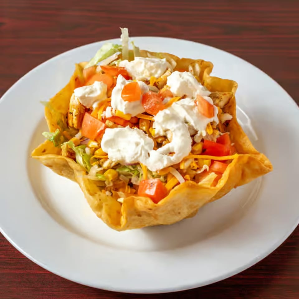 A taco salad in a crispy tortilla bowl, topped with sour cream, tomatoes, and cheese.