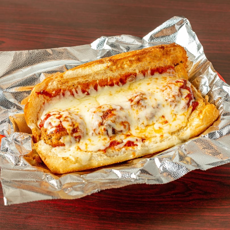 A Topolino's meatball sub, generously covered in melted mozzarella cheese and marinara sauce, in foil.