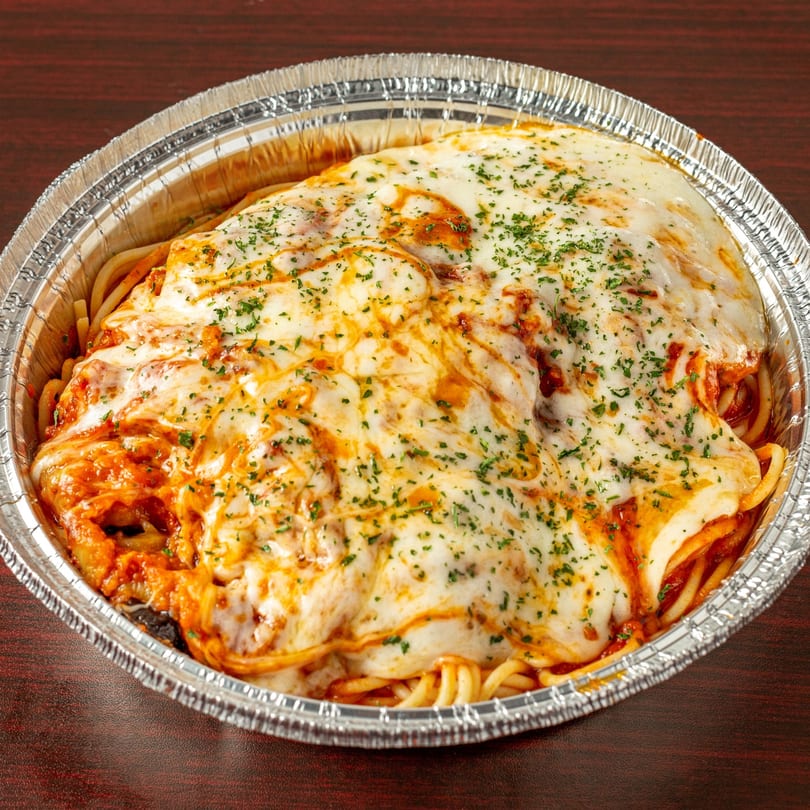 Baked spaghetti with melted mozzarella cheese and parsley in a foil takeout container.